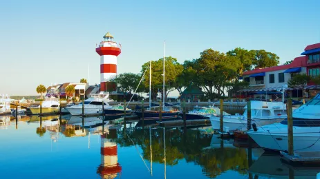small boats moored along a pier with a red and white striped lighthouse in the distance