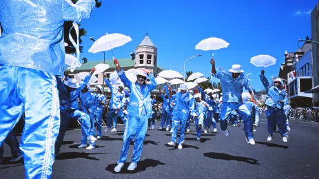 A parade of men in blue and white suites, with white umbrellas, in lively celebration