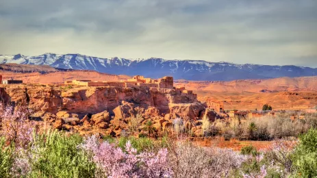 A small town resting on a rocky outcrop against the backdrop of the snowy Atlas Mountains