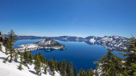 Pristine Lake surrounded by snowy, hilly terrain against a blue sky