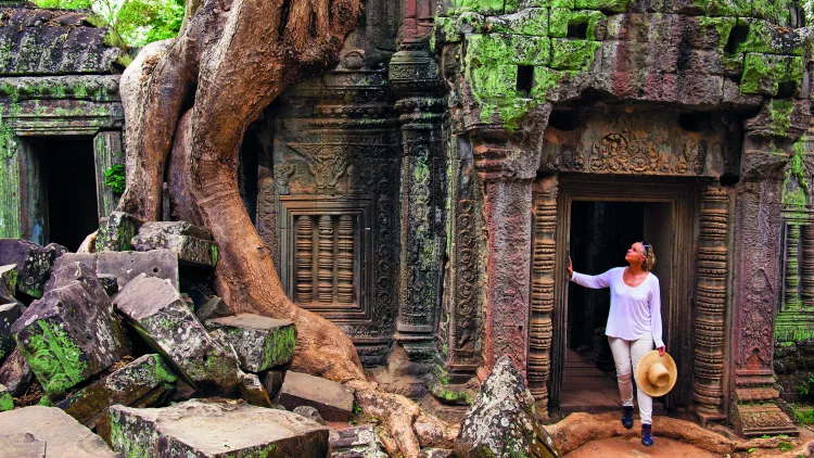 A Woman paused in the doorway of an ancient ruin of Ta Prohm, looking in up in admiration.