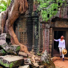 A Woman paused in the doorway of an ancient ruin of Ta Prohm, looking in up in admiration.