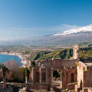 Taormina theatre columns with snowy Mount Etna in the distance in Taormina, Italy