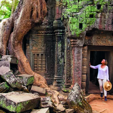 A Woman paused in the doorway of an ancient ruin of Ta Prohm, looking in up in admiration.