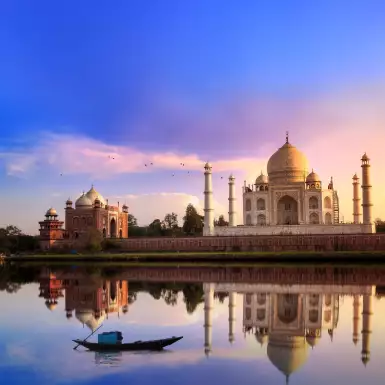 View of the Taj Mahal at sunset, it's image reflected in the water of a foreground lake.