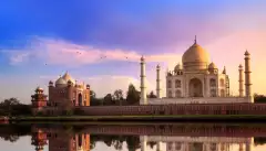 View of the Taj Mahal at sunset, it's image reflected in the water of a foreground lake.