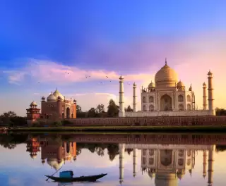 View of the Taj Mahal at sunset, it's image reflected in the water of a foreground lake.