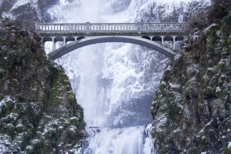 white bridge connected with cliff sides in front of a white, partly frozen waterfall